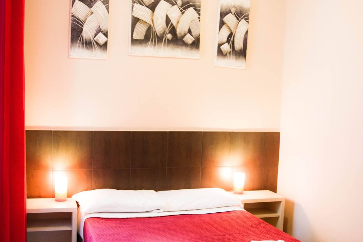 A hotel room with a bed, two bedside tables, a nightstand, and three wall-mounted artworks.