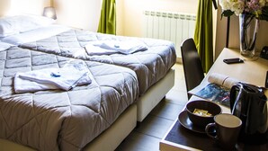 A hotel room with a bed, a desk with a coffee maker, a vase with flowers, and a window with curtains. - Mosaic Guest House (Rome)