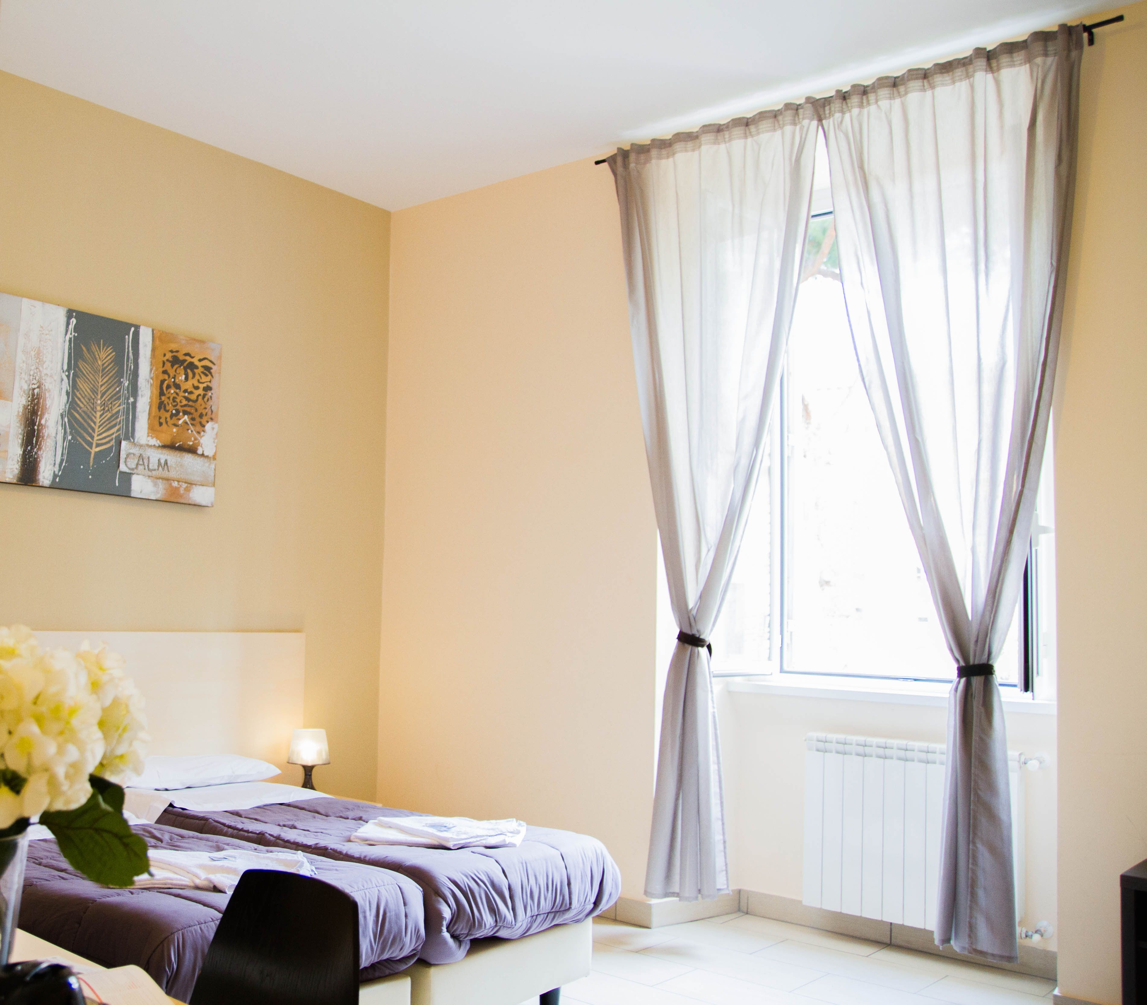 A bedroom with a bed, a desk, a lamp, and a window with curtains.