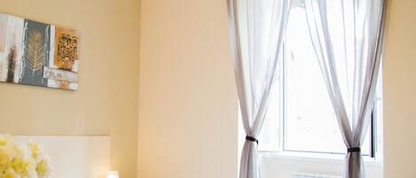 A bedroom with a bed, a desk, a lamp, and a window with curtains.