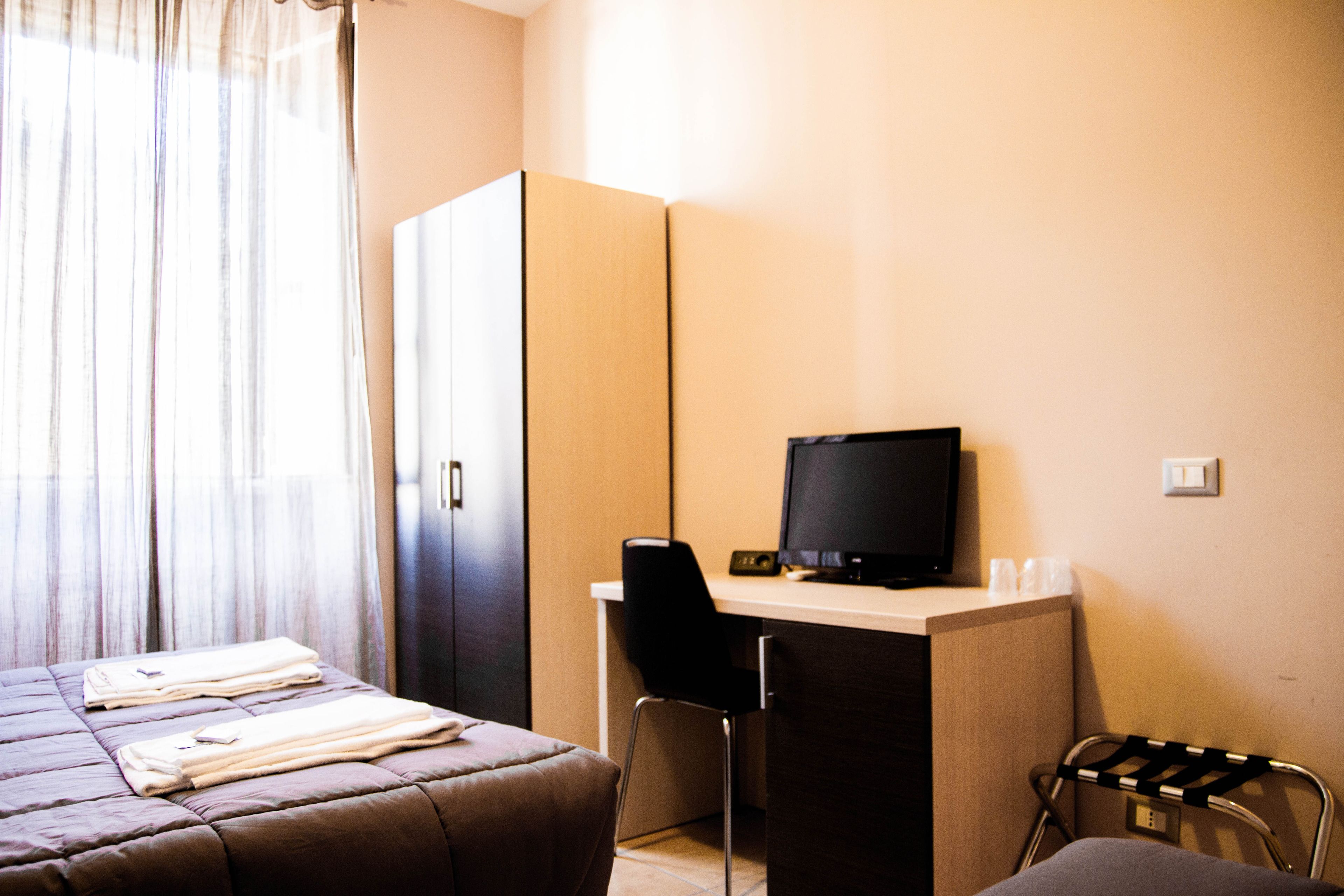 A hotel room with a bed, a desk with a computer, a chair, and a wardrobe.