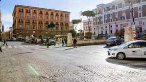 A cobblestone street with historic buildings, a white car, and pedestrians. - Mosaic Guest House (Rome)