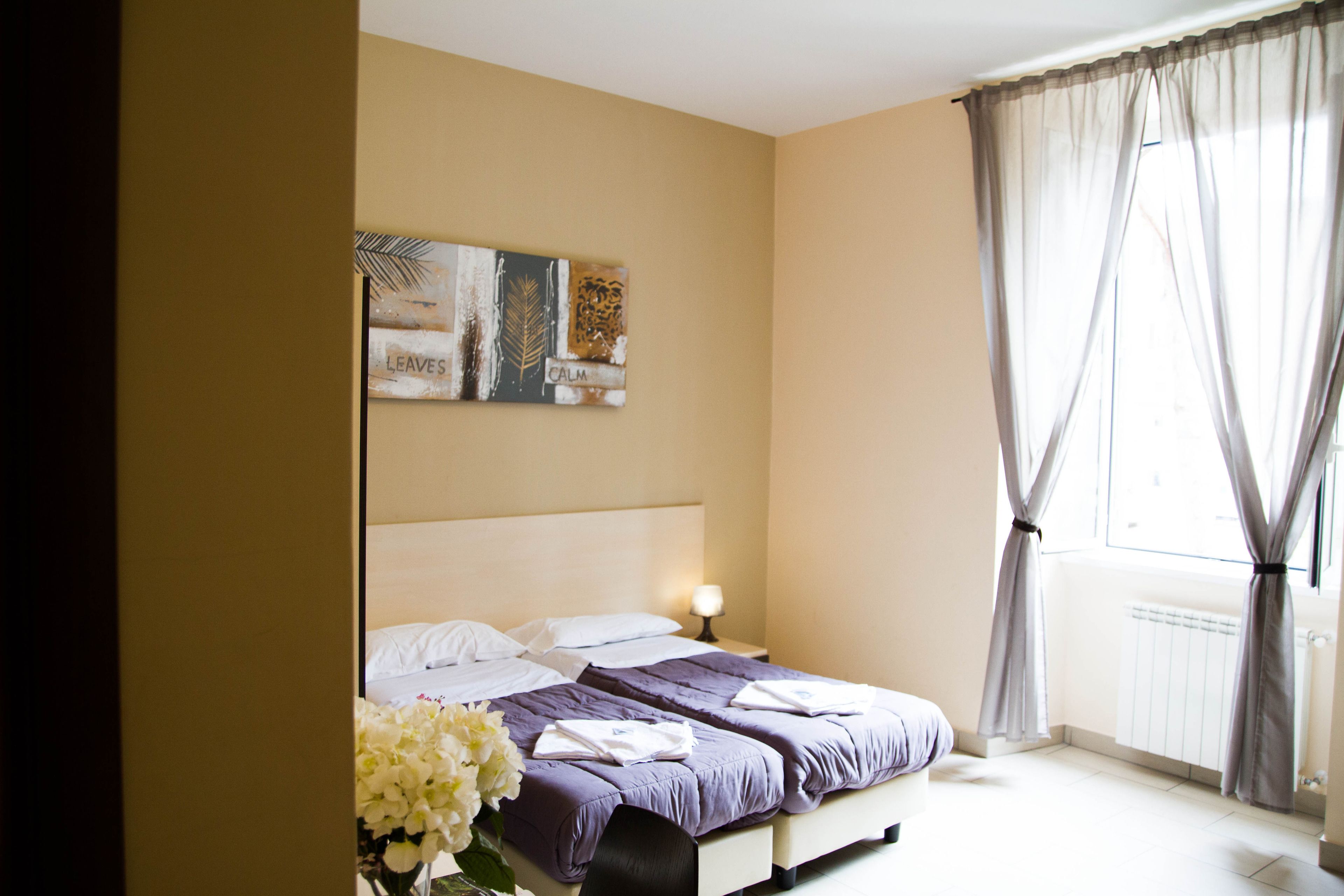 A neatly made bed with a headboard, a bedside table with a lamp, and a window with curtains.