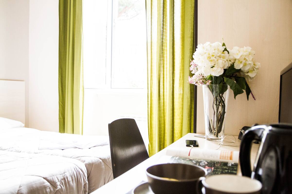 A hotel room with a bed, a desk with a vase of flowers, a chair, and a coffee maker.