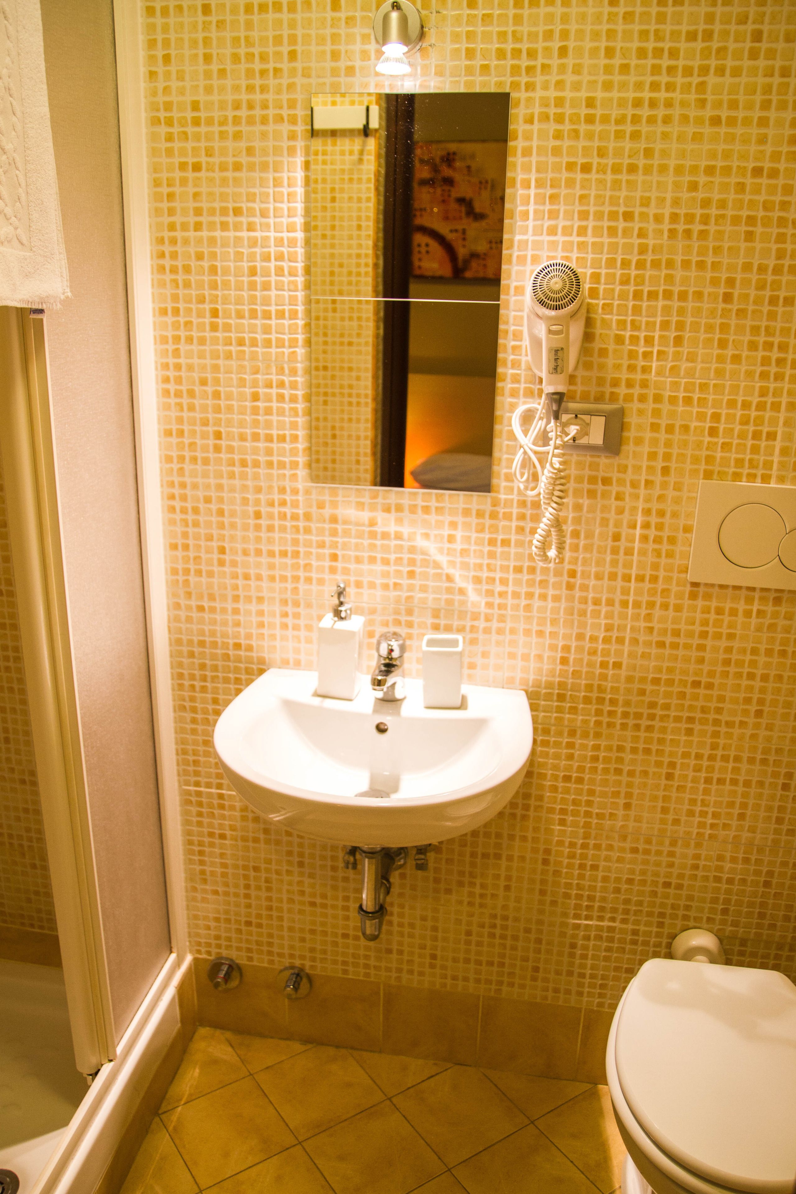 Une salle de bain équipée d’un lavabo, d’un miroir et d’un sèche-cheveux fixé au mur.