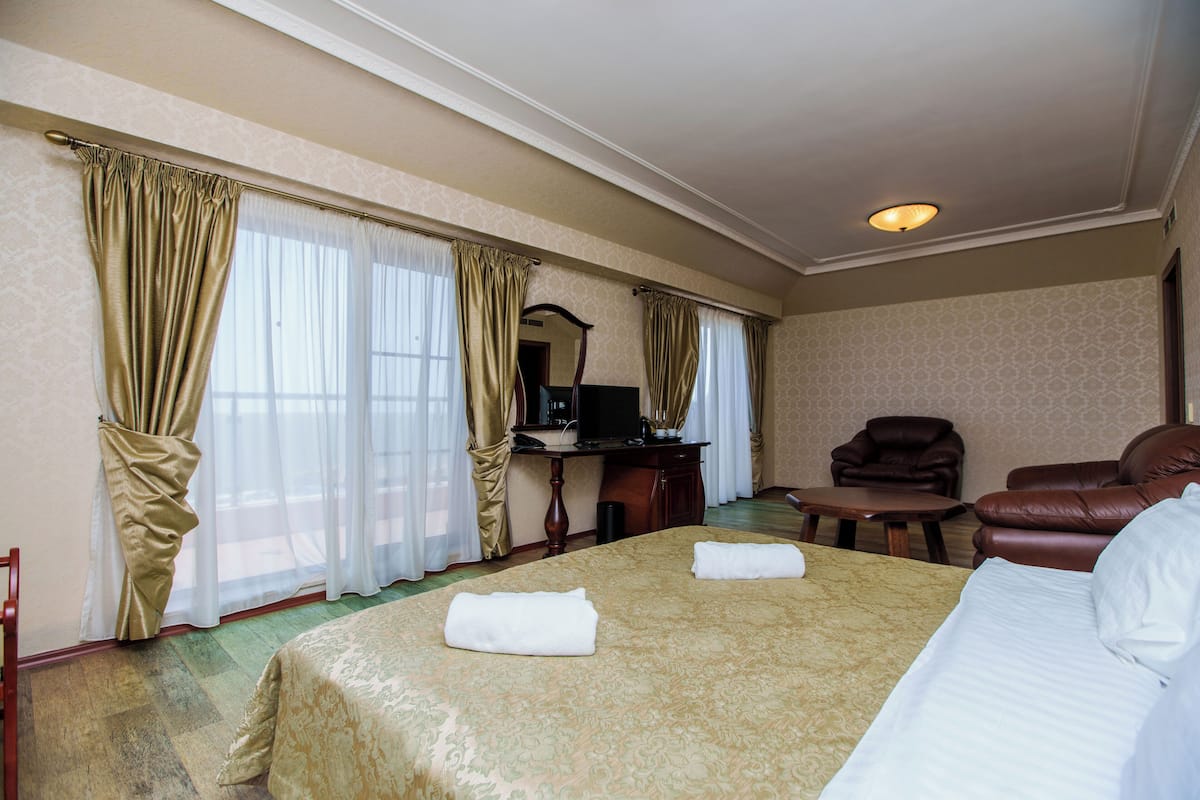 A hotel room with a large bed, two armchairs, a desk with a computer, and a mirror.