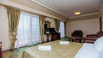 Una habitación de hotel con una cama grande, dos sillones, un escritorio con computadora y un espejo.