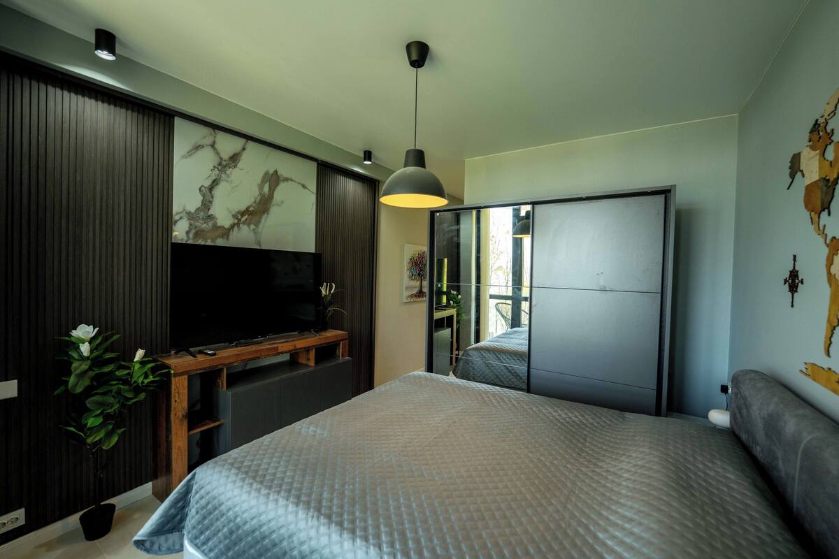 A modern bedroom with a bed, a TV, a desk, and a wardrobe.