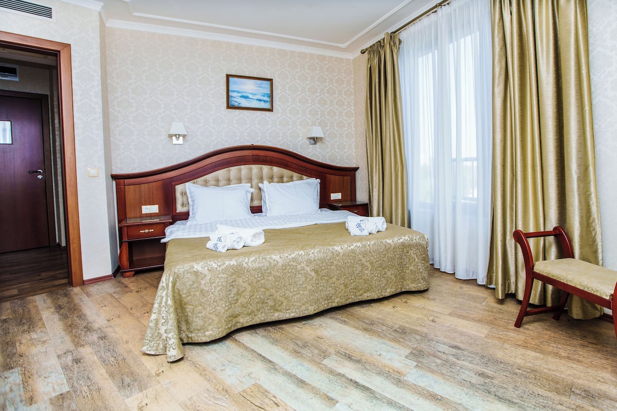 A hotel room with a wooden bed, a wooden chair, a nightstand, and a picture on the wall.