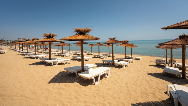 A beach with rows of white sun loungers and thatched umbrellas, offering a clear view of the sea. - Aqua View Spa Boutique Hotel (Varna)