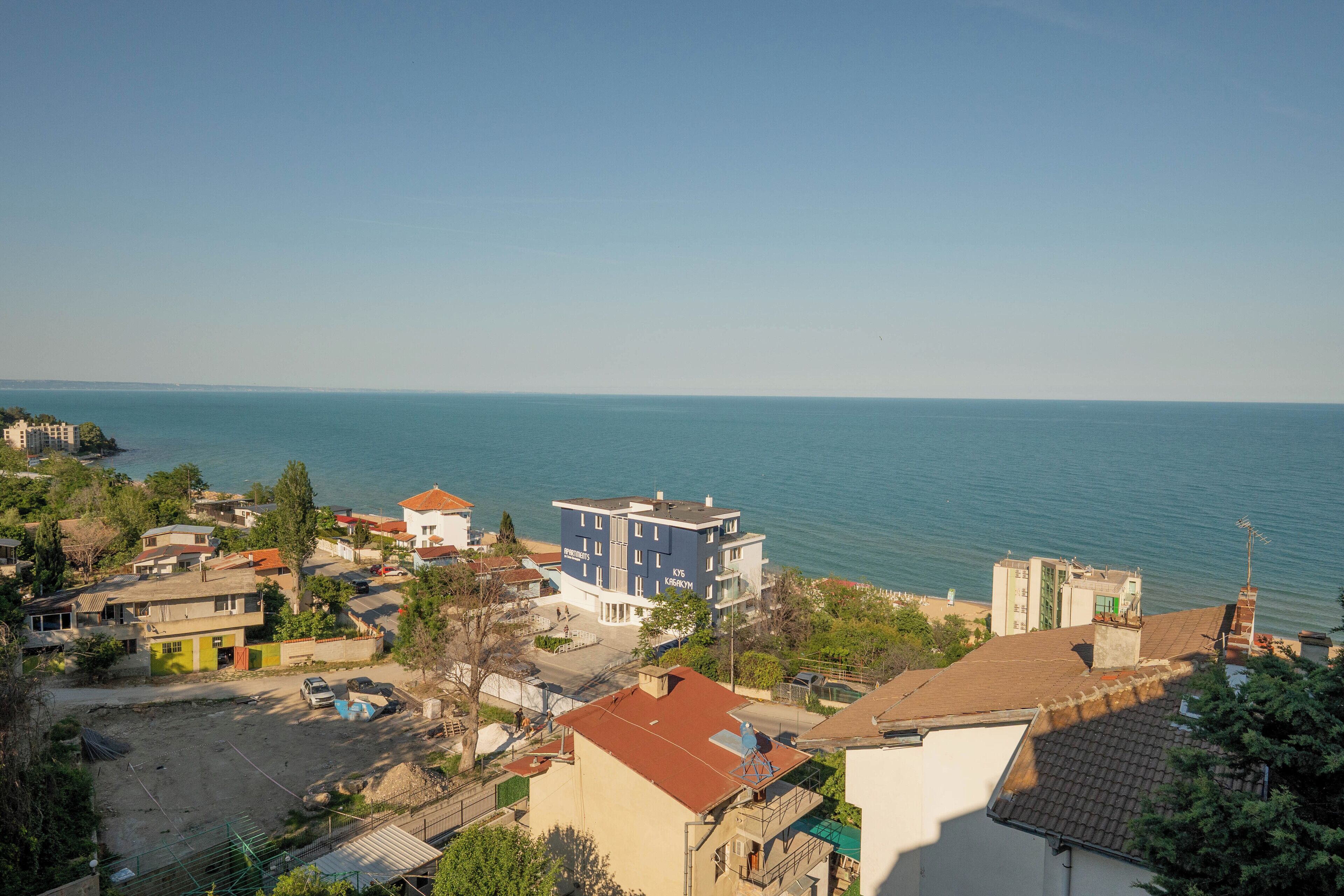 Zona residencial costera con edificios, vista despejada al mar y un estacionamiento.