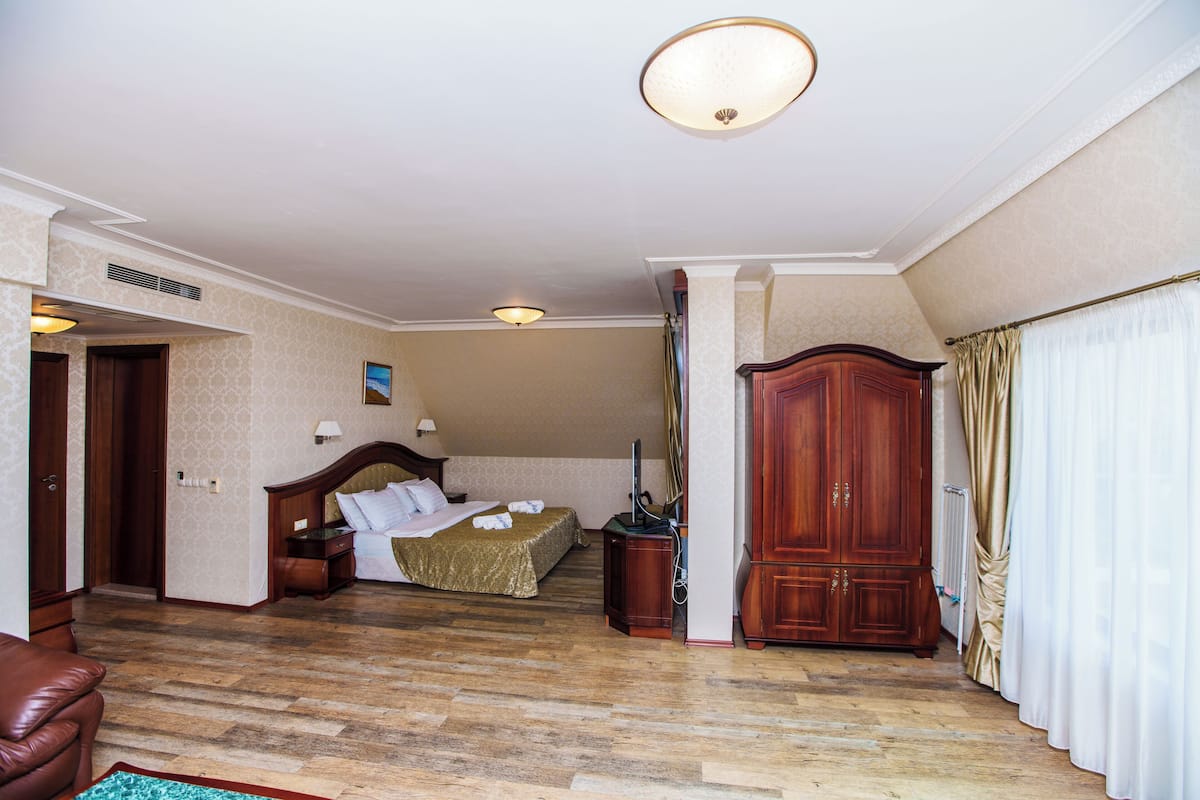 A hotel room with a wooden floor, a bed with a headboard, a wardrobe, a desk, and a chair.