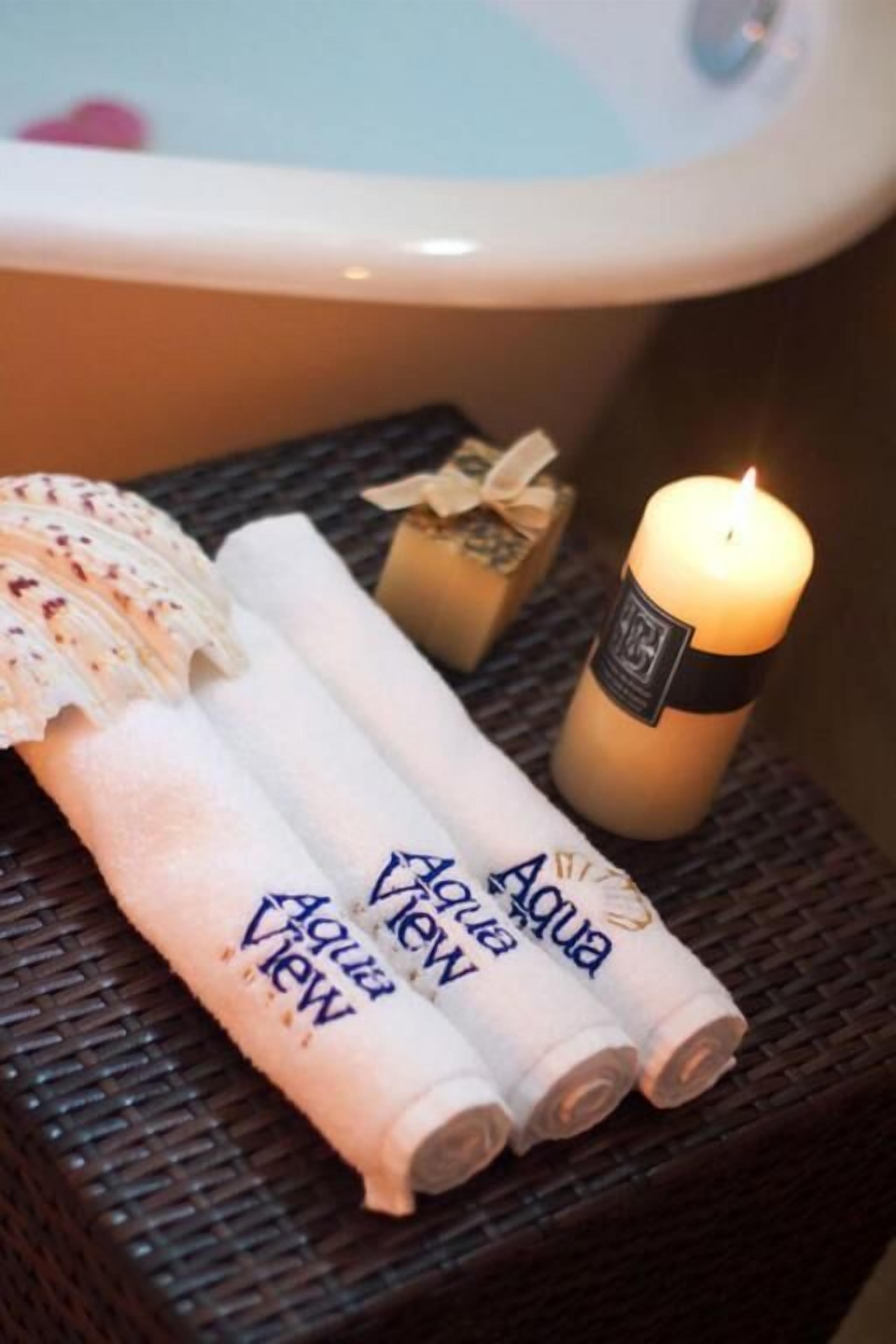 A bathroom with a bathtub, a lit candle, rolled towels, and a seashell.