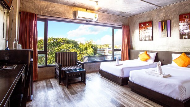 Une chambre d’hôtel avec deux lits, un bureau, une chaise et une grande fenêtre donnant sur la ville.