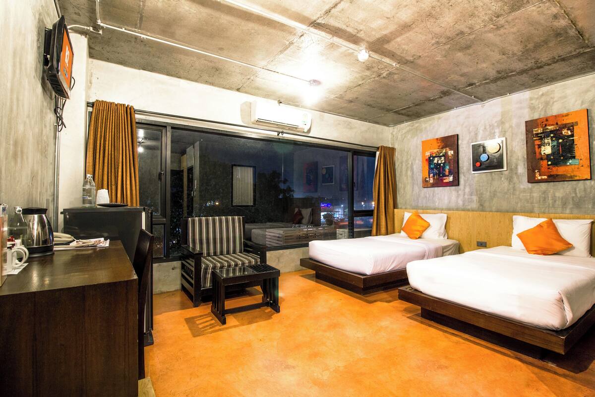Habitación de hotel con dos camas, un escritorio, una silla y un ventanal con cortinas.