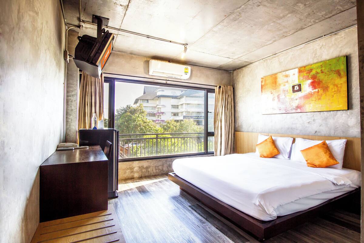 Una habitación de hotel con cama, escritorio, ventana y un cuadro en la pared.