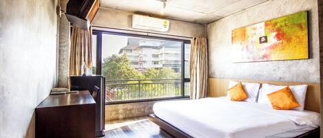 A hotel room with a bed, a desk, a window, and a painting on the wall.