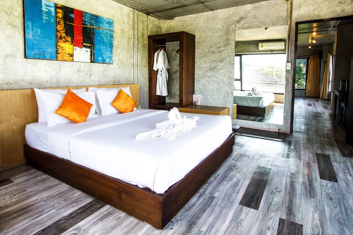 Habitación de hotel con una cama grande, cabecera de madera y vista al baño a través de una puerta de vidrio.