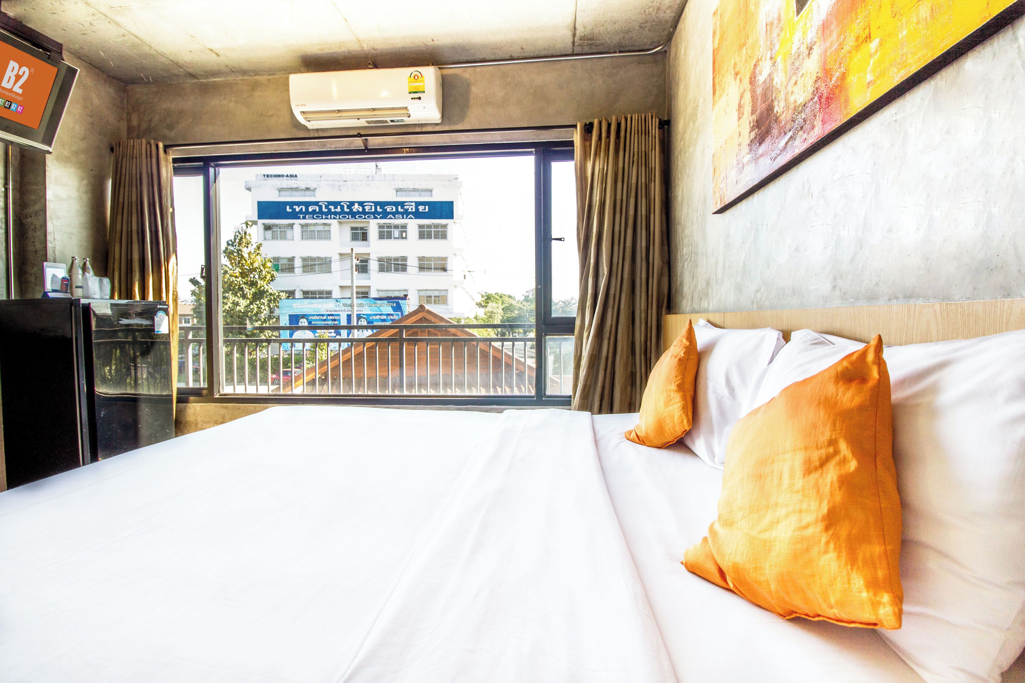 Une chambre d’hôtel avec un grand lit, une fenêtre donnant sur un immeuble et un ventilateur de plafond.