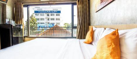 Una habitación de hotel con una cama grande, un ventanal con vistas a un edificio y un ventilador de techo.