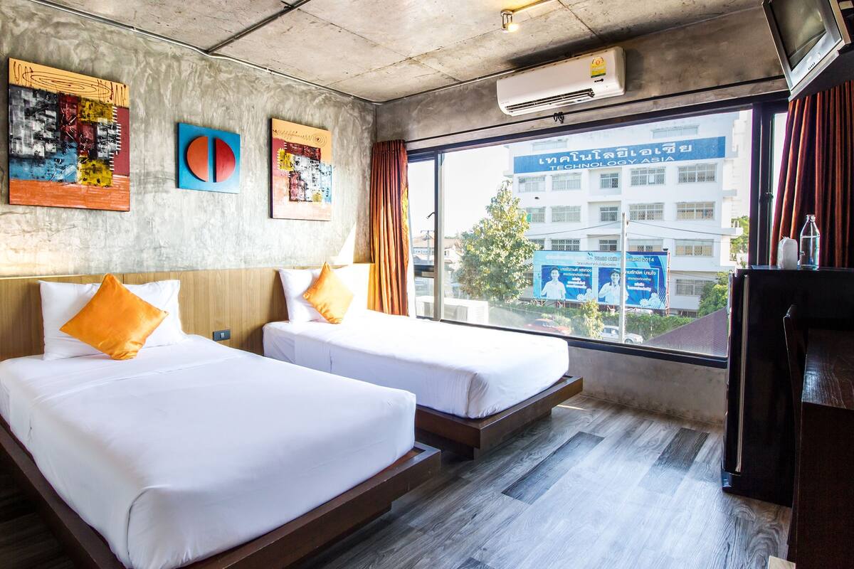 Habitación de hotel con dos camas, una ventana que ofrece vistas a un edificio y obras de arte en la pared.