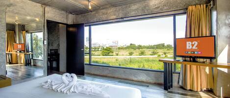 A modern hotel room with a large bed, a TV, and a view of a green landscape.