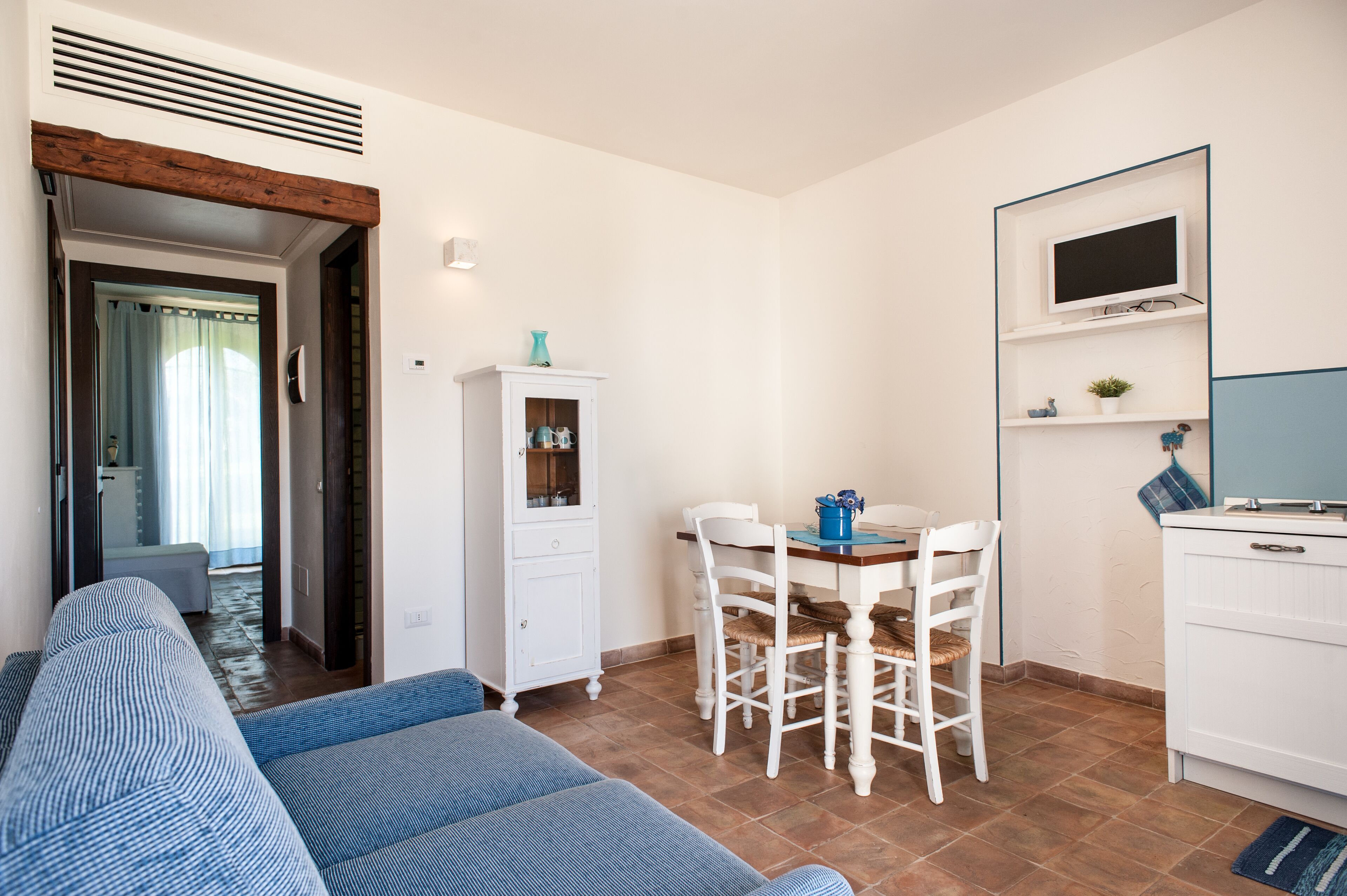 A compact living space with a sofa, a dining table with chairs, a cabinet, and a television mounted on the wall.