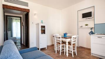 A compact living space with a sofa, a dining table with chairs, a cabinet, and a television mounted on the wall.