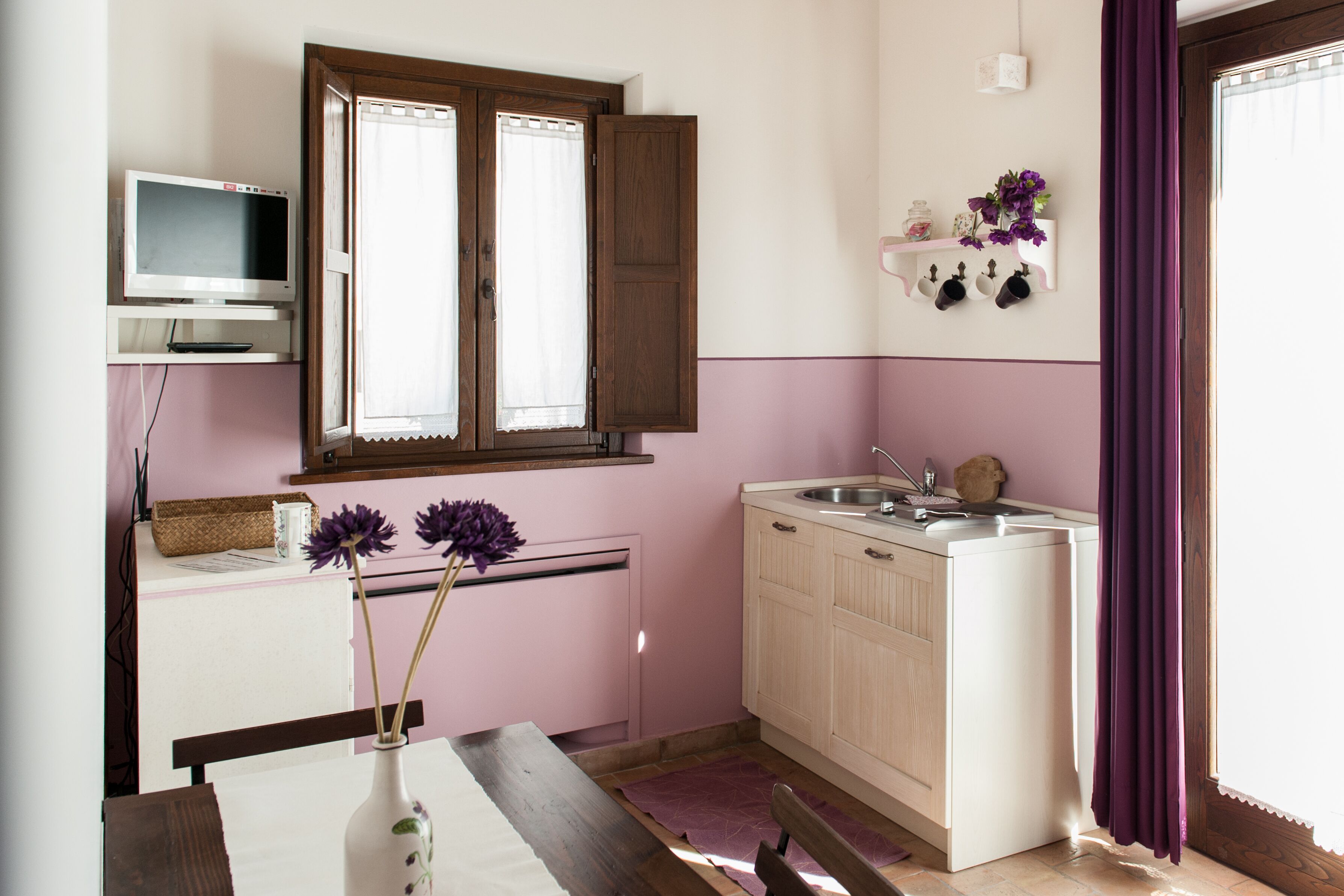 Cocina compacta con horno integrado, un lavamanos pequeño y una ventana con contraventanas de madera.