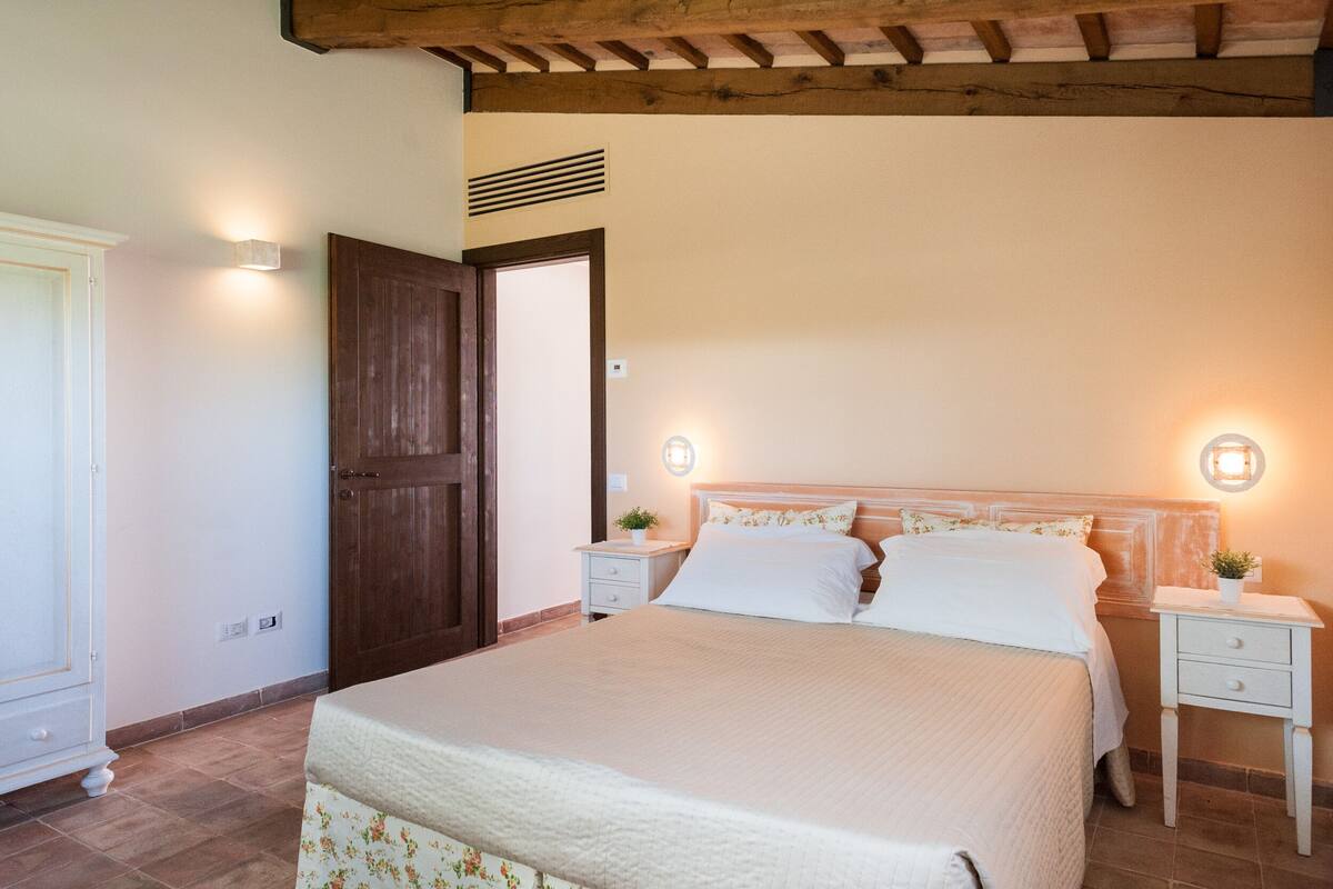 A bedroom with a large bed, two bedside tables, a wooden door, and a wall-mounted light fixture.