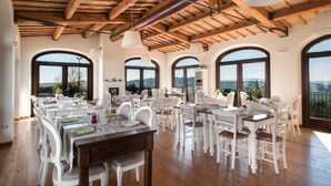 A dining area with wooden beams, white furniture, and large arched windows offering a view. - Villa Coralia (Osimo)