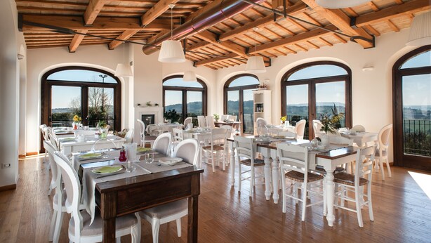 A dining area with wooden beams, white furniture, and large arched windows offering a view. - Villa Coralia (Osimo)