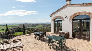 A patio with outdoor furniture, a view of the countryside, and a building with arched windows and a chimney. - Villa Coralia (Osimo)