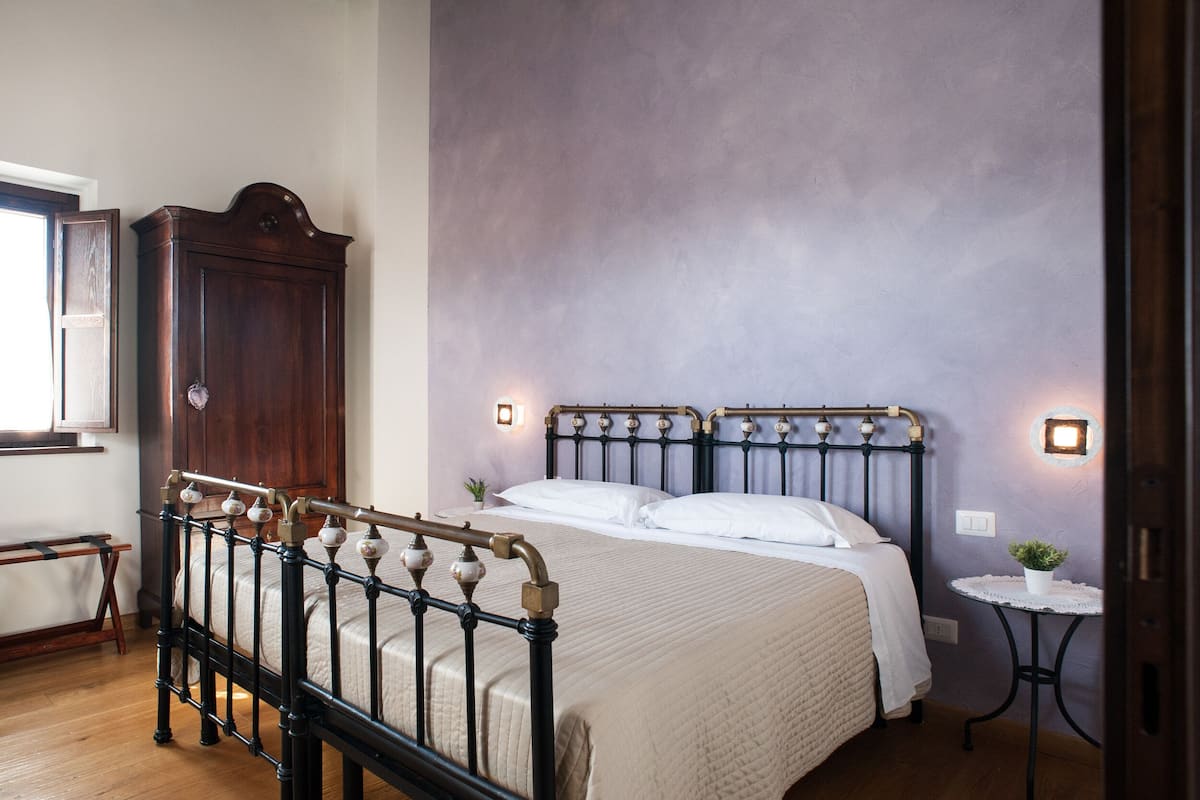 A bedroom with a bed, wooden wardrobe, and a small round table with a plant.