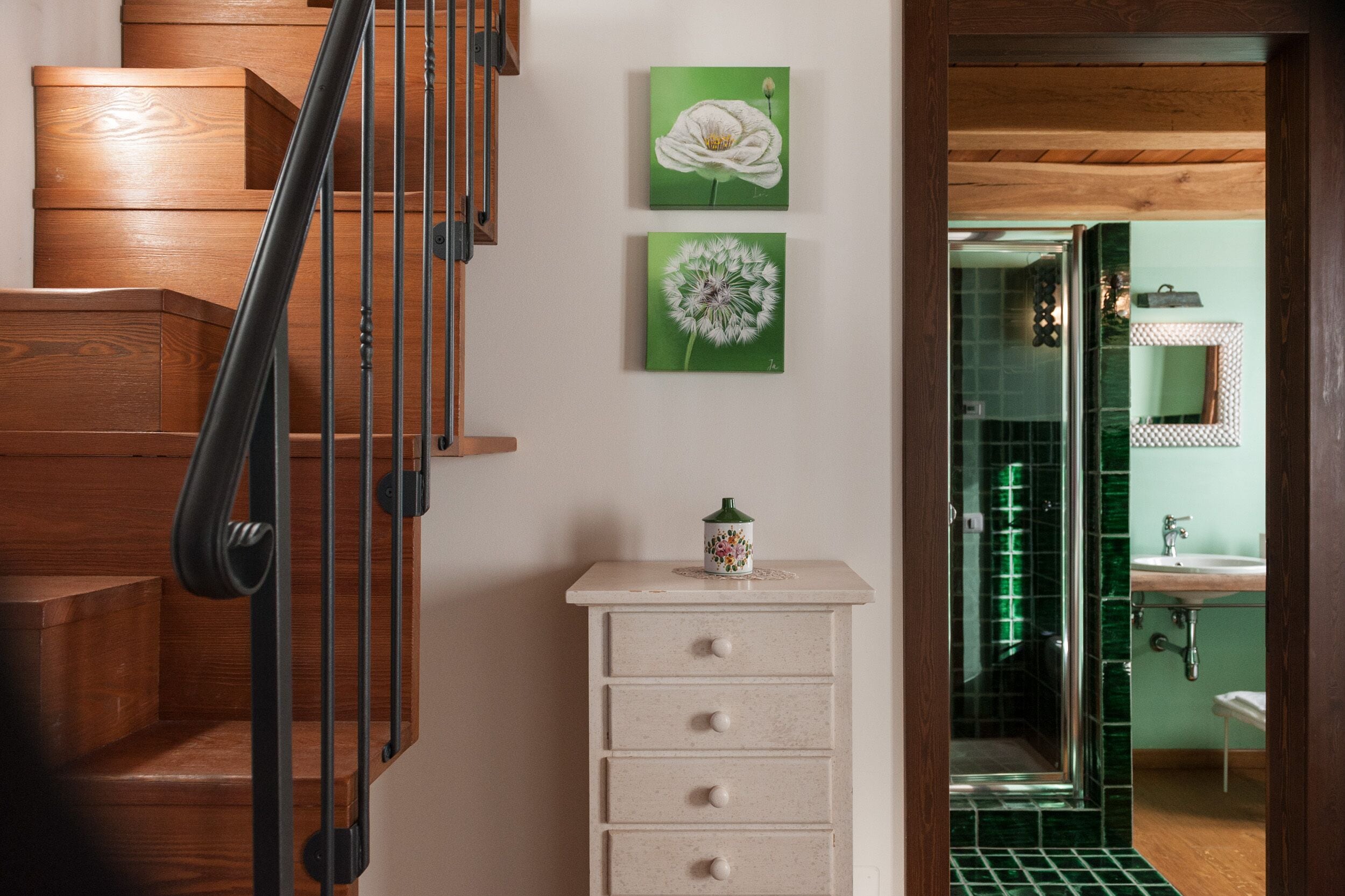Un escalier en bois, agrémenté d’une petite armoire et de deux tableaux floraux encadrés.