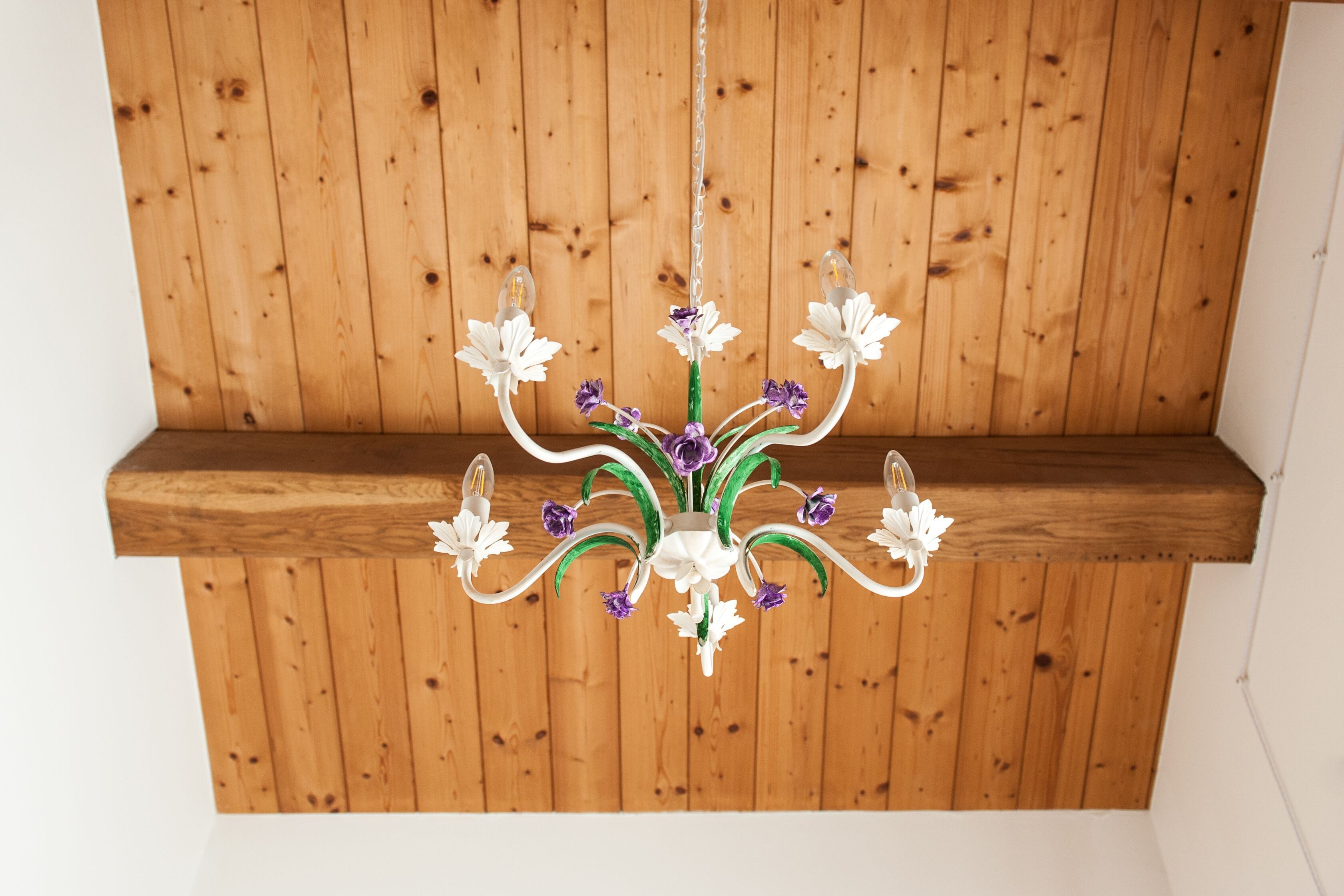 Een kroonluchter met bloemmotieven aan een houten plafond.