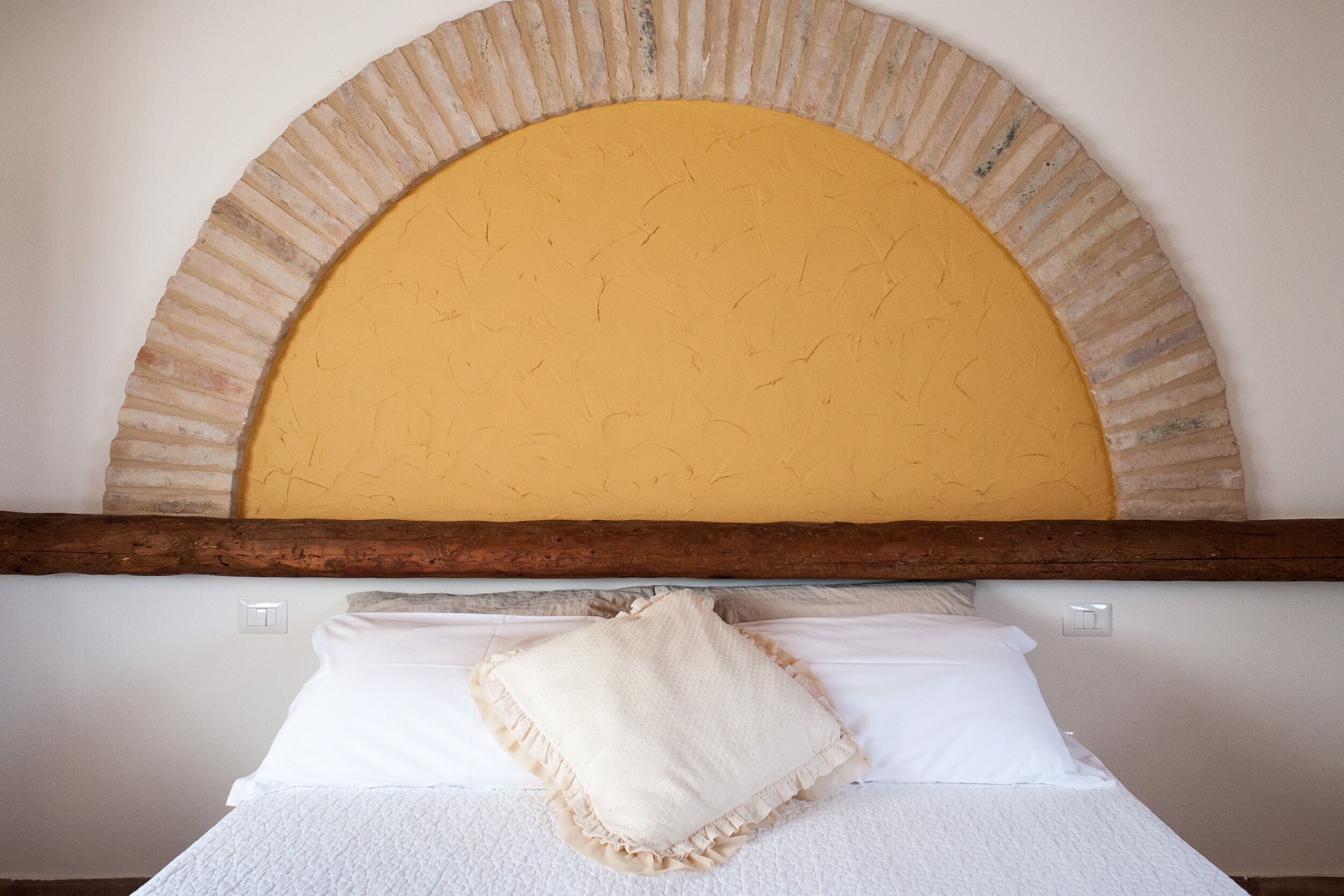 Una cama con ropa de cama blanca, una almohada color beige y un cabecero de madera con un arco amarillo.