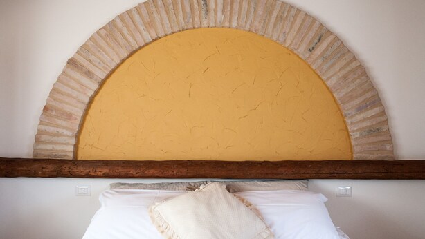 A bed with white bedding, a beige pillow, and a wooden headboard with a yellow arch. - Villa Coralia (Osimo)