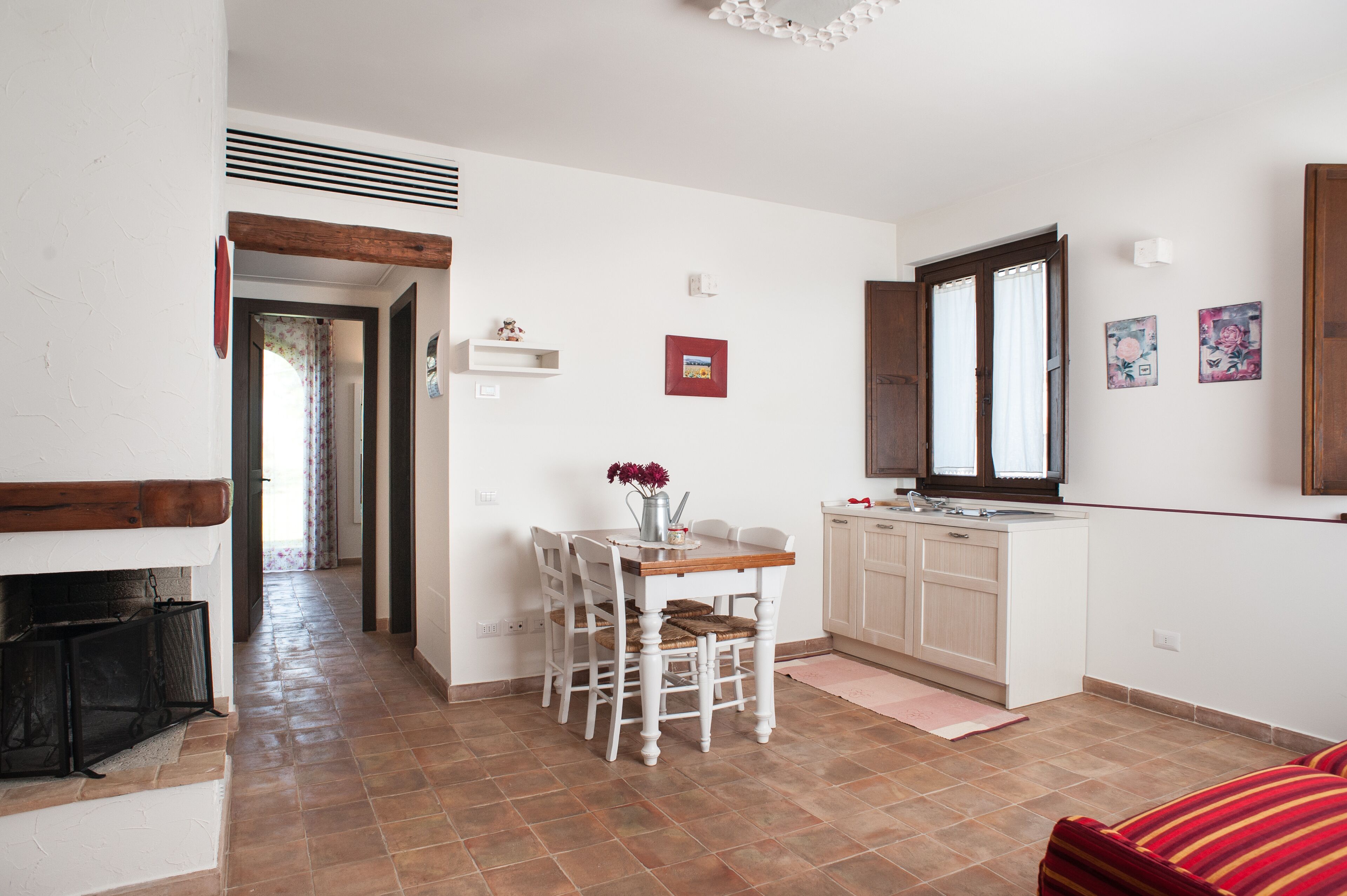 Cucina compatta con mobili bianchi, un tavolo da pranzo con sedie e una finestra con tende.