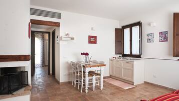Cucina compatta con mobili bianchi, un tavolo da pranzo con sedie e una finestra con tende.