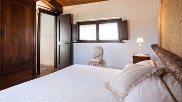 Un dormitorio con una cama grande, un armario de madera, una silla, una mesita de noche con una lámpara y una ventana con persianas.