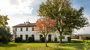 A white building with a tiled roof, arched windows, and a tree with orange leaves in the foreground. - Villa Coralia (Osimo)