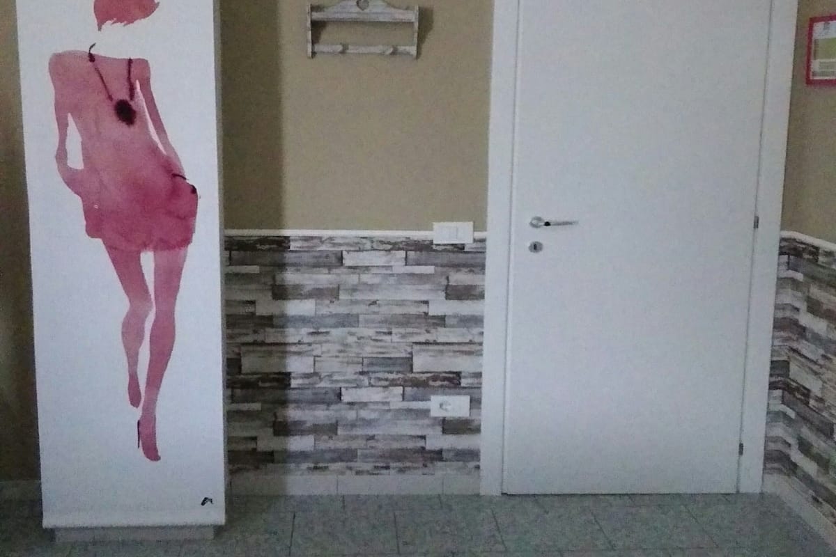 Een kamer met betegelde vloer, een witte deur, een wandplank en een groot roze silhouetkunstwerk.