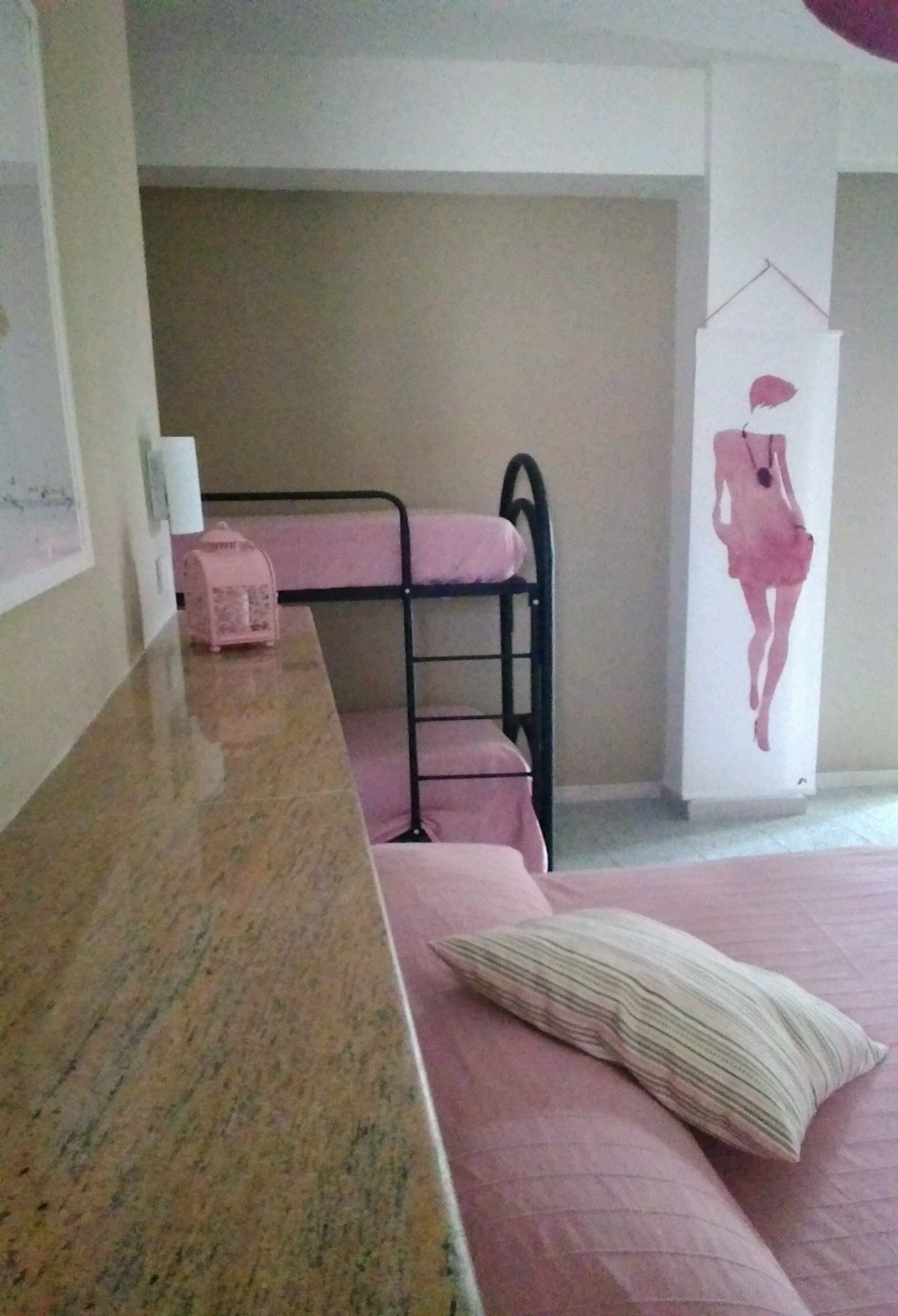 En våningssäng med en rosa madrass och en enkelsäng med en randig kudde.