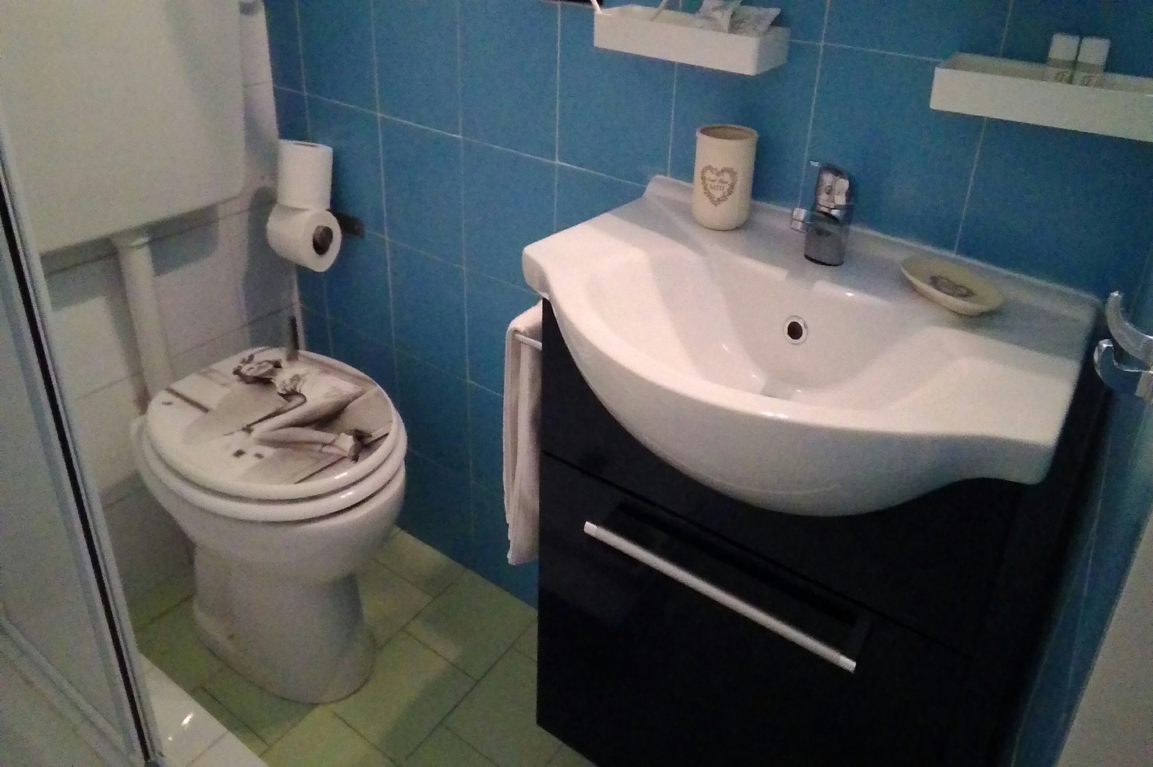 A bathroom with a toilet, a sink, and a blue tiled wall.