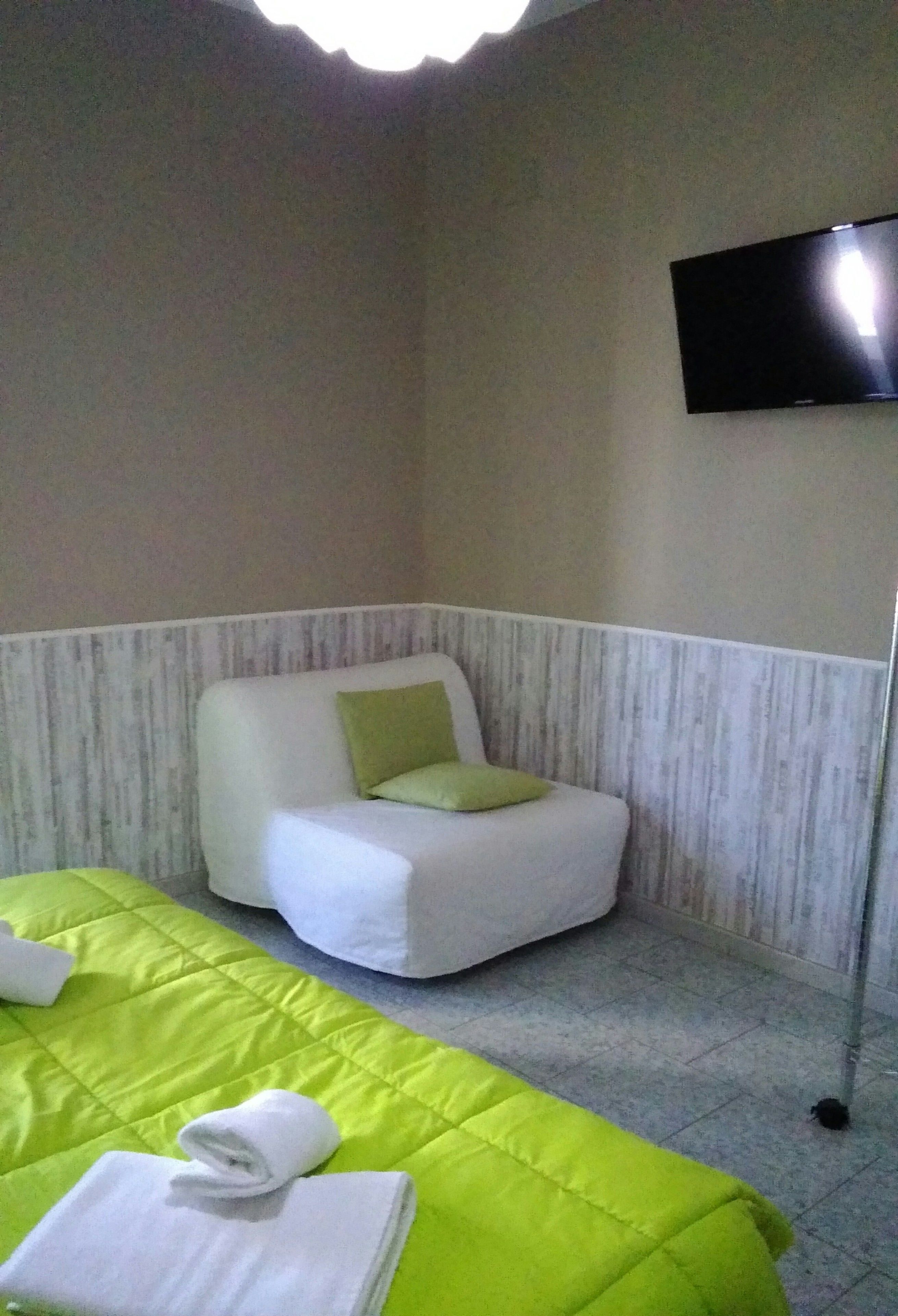 A small, cozy room with a single bed, a chair, and a flat-screen TV mounted on the wall.