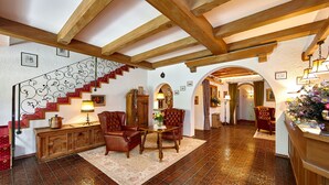A spacious living area with a wooden staircase, a fireplace, and a dining table with chairs. - Gästehaus Franziska (Mittenwald)