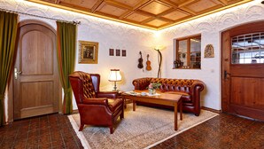A traditional room with a wooden ceiling, a large wooden door, a leather sofa, a wooden coffee table, and a patterned rug. - Gästehaus Franziska (Mittenwald)