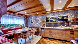 A cozy kitchen with wooden cabinets, a dining area with a red bench, and a stone backsplash. - Gästehaus Franziska (Mittenwald)