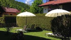 A garden with two white umbrellas, a wooden house, and a mountain backdrop. - Gästehaus Franziska (Mittenwald)